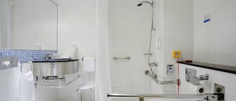 Une salle de bain moderne équipée d’une douche, de toilettes et d’un lavabo, ainsi que de barres d’appui et d’un siège accessible aux personnes en fauteuil roulant.