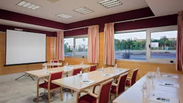 A conference room with a whiteboard, tables, chairs, and large windows with curtains.