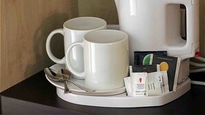 Une machine à café, accompagnée de deux tasses blanches et d’une cuillère sur un plateau, ainsi qu’un paquet de capsules de café.