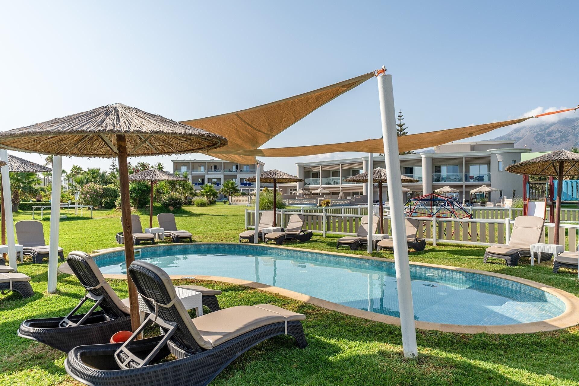 A swimming pool with lounge chairs and umbrellas, surrounded by a well-maintained lawn and a building in the background.