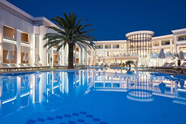 A hotel with a large indoor pool, palm trees, and a modern building with balconies.