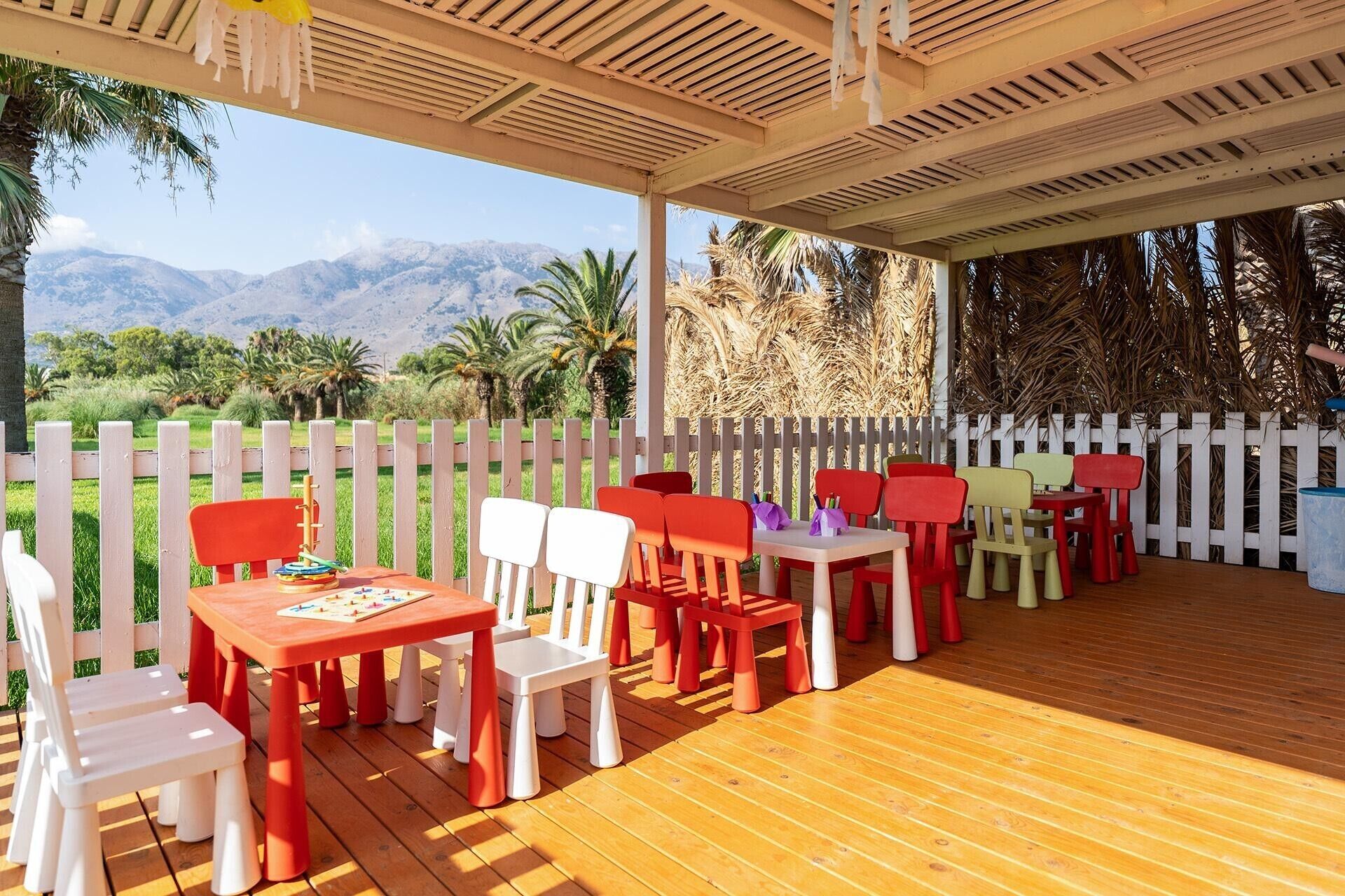An outdoor patio with wooden flooring, white and red chairs, and tables.