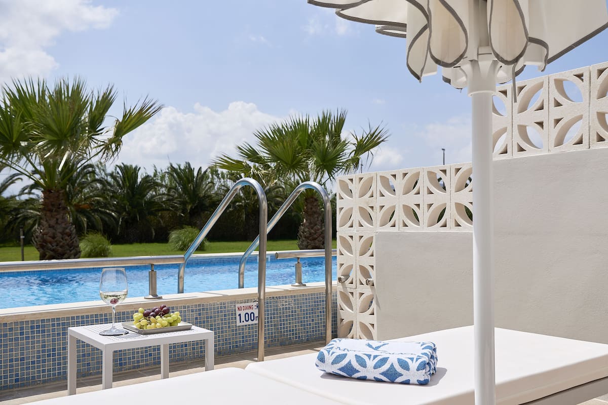 A poolside lounge with a glass table, a towel, and a glass of wine.