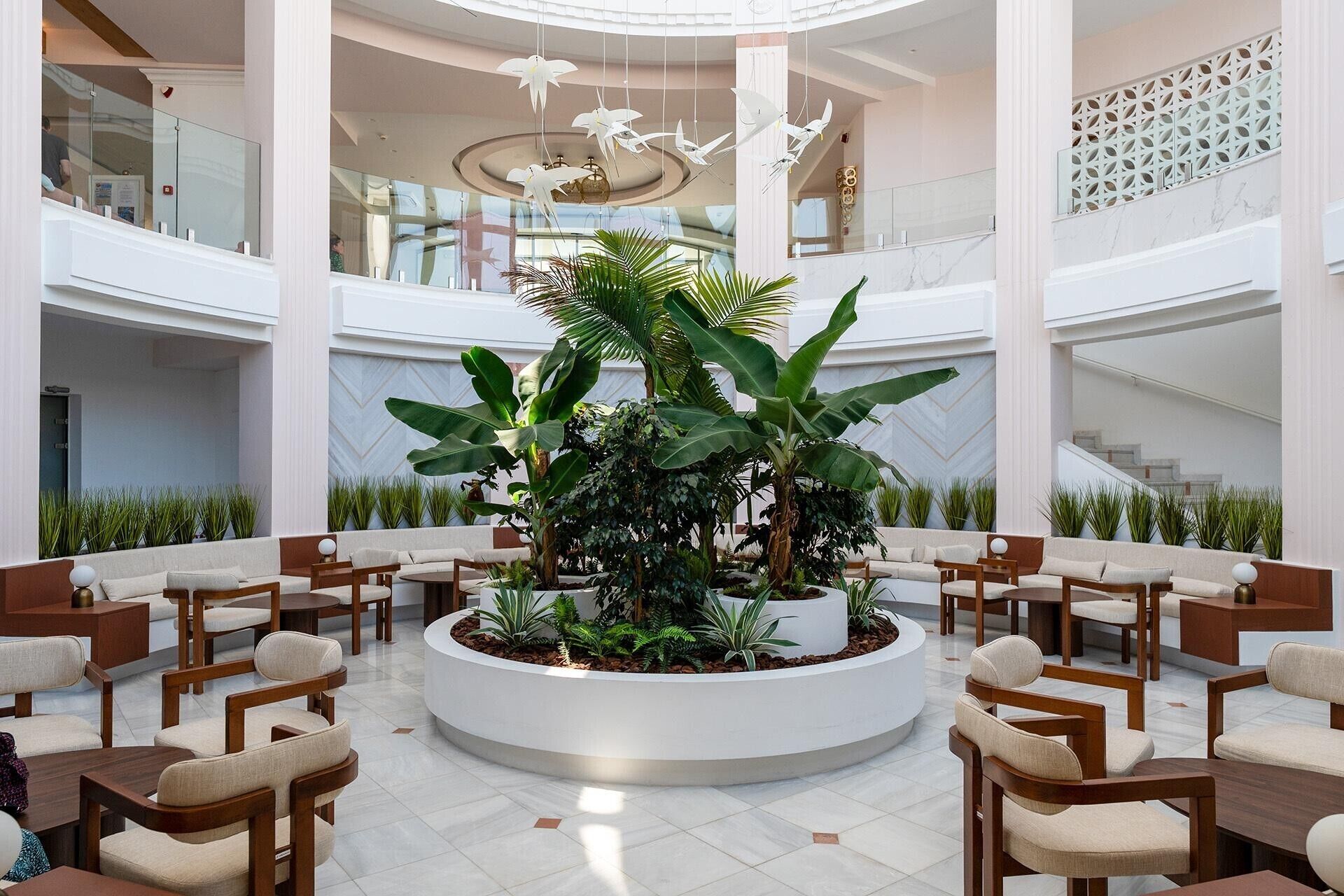 A spacious lobby with a central planter, multiple seating areas, and a staircase in the background.