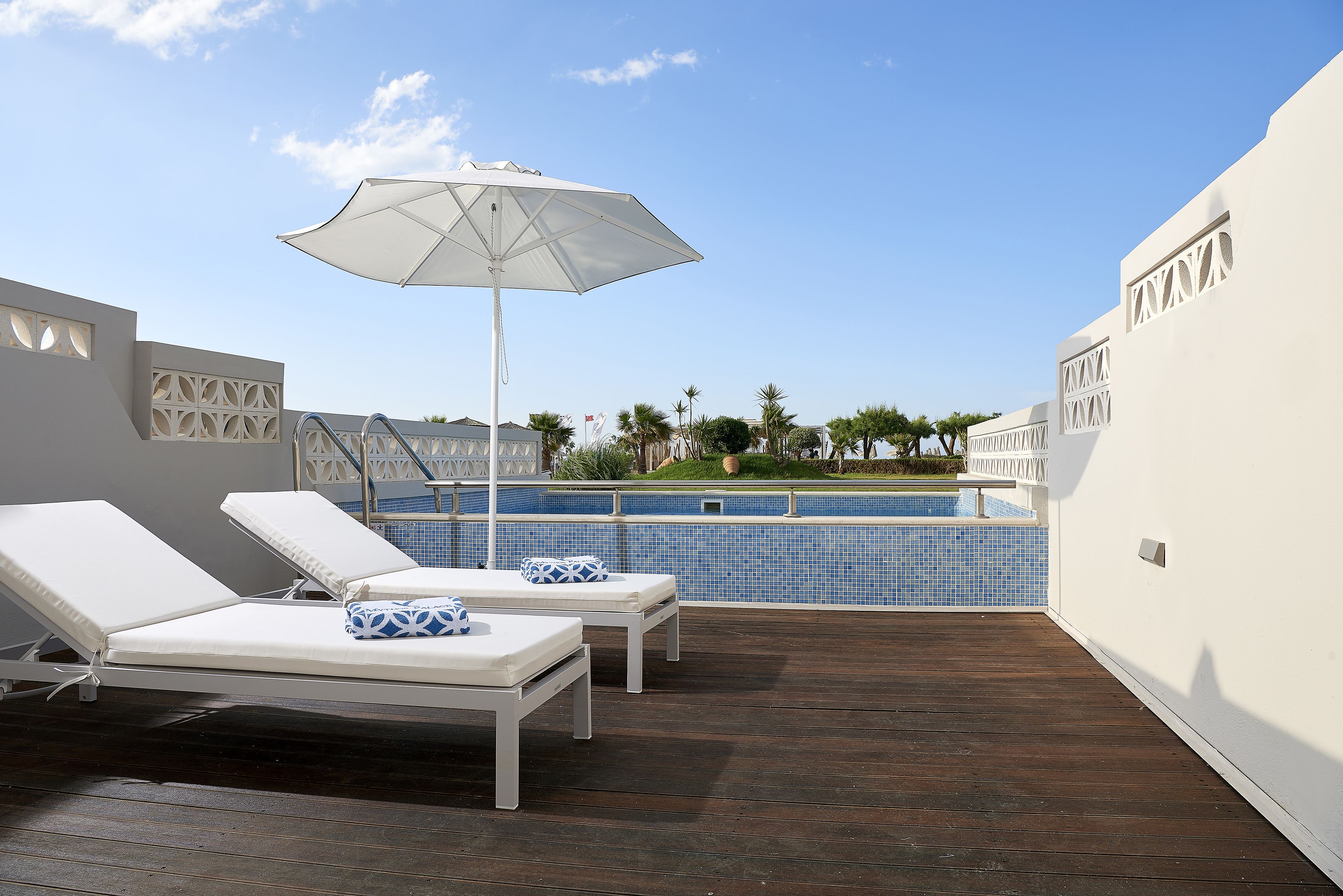 A rooftop pool area with two sun loungers and a large umbrella.