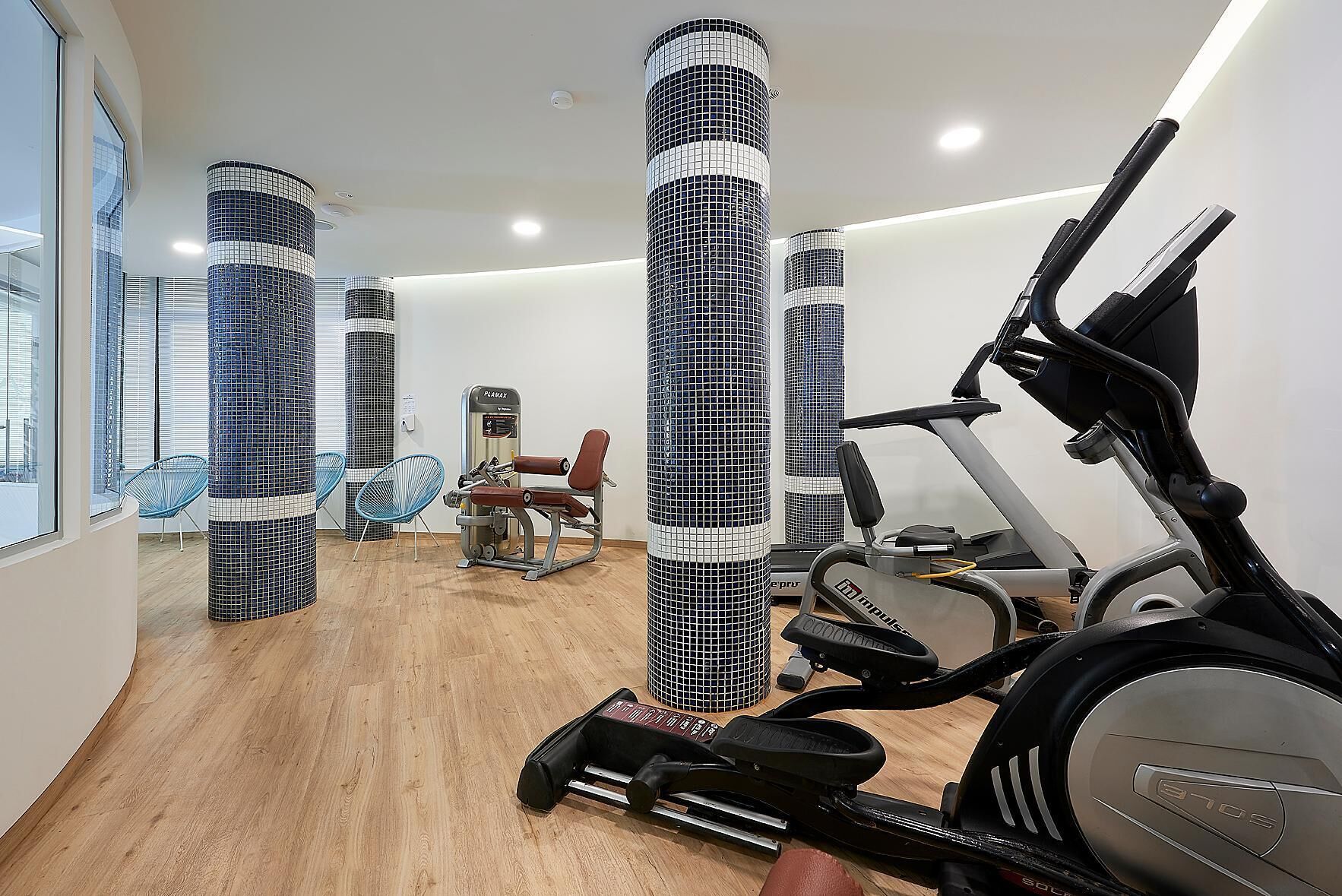 Et fitnesscenter med træningsudstyr, spejlvægge og trægulv.