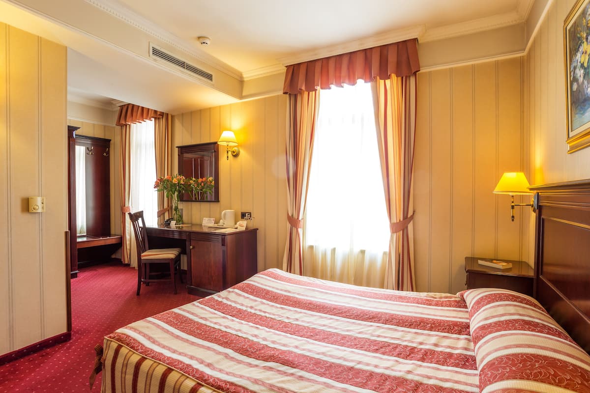 A hotel room with a large bed, a desk, a chair, and a nightstand with a lamp.