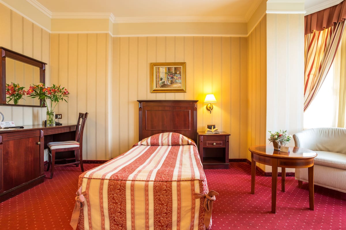 A hotel room with a bed, a desk with a chair, a small table with a lamp, and a sofa.
