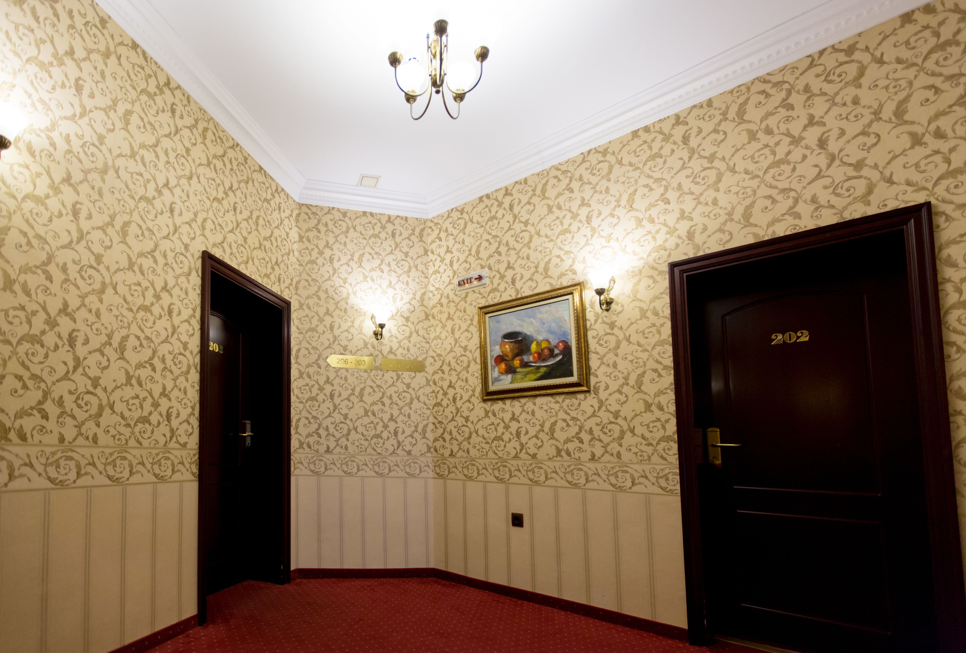 Een hotelkamer met behang met patroon, een kroonluchter, twee deuren en een schilderij aan de muur.