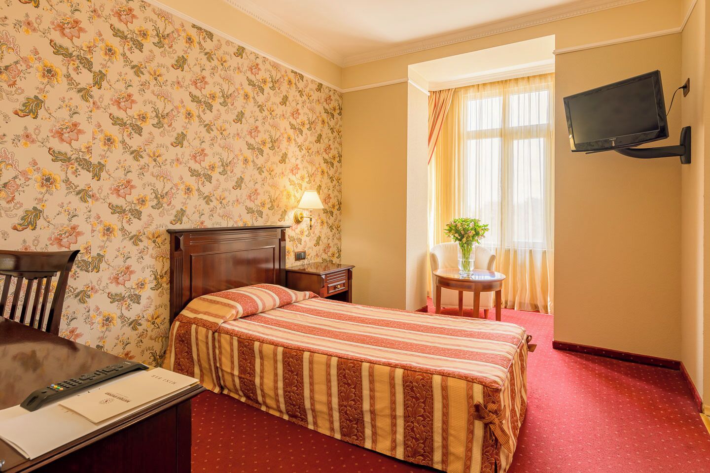 A hotel room with a bed, a desk, a chair, a television, and a window with curtains.