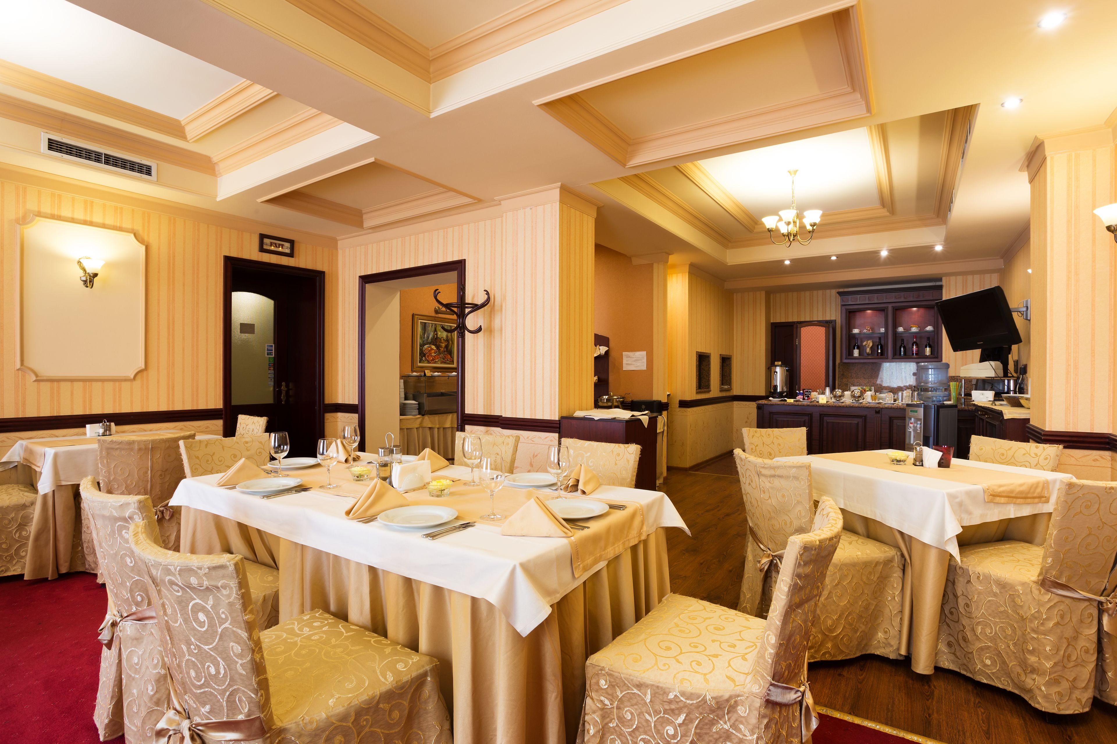 A dining area with tables set for service, chairs with patterned covers, and a bar area in the background.