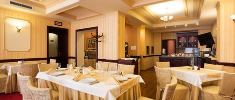A dining area with tables set for service, chairs with patterned covers, and a bar area in the background.