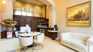 A hotel lobby with a reception desk, a dining area with a round table and chairs, a white sofa, and a painting on the wall. - Boutique Splendid Hotel (Varna)