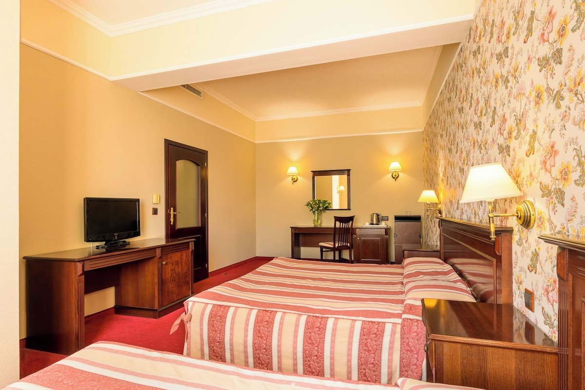 A hotel room with two beds, a desk, a television, and a mirror.
