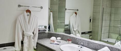A modern bathroom with a white toilet, a sink with a mirror above it, and a towel rack with two white robes.