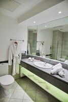 Un baño moderno con inodoro blanco, un lavamanos con espejo y un perchero con dos albornoces blancos.