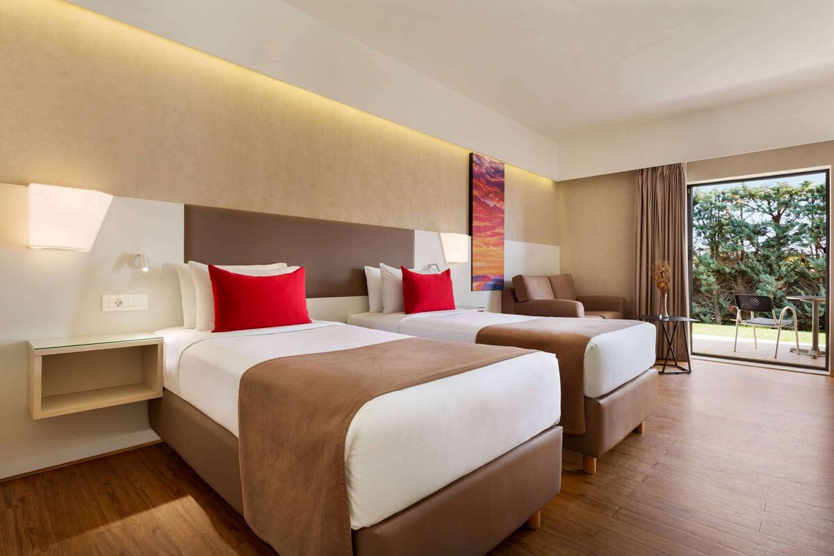A hotel room with two beds, a sofa, a small table, and a view of the outdoors.