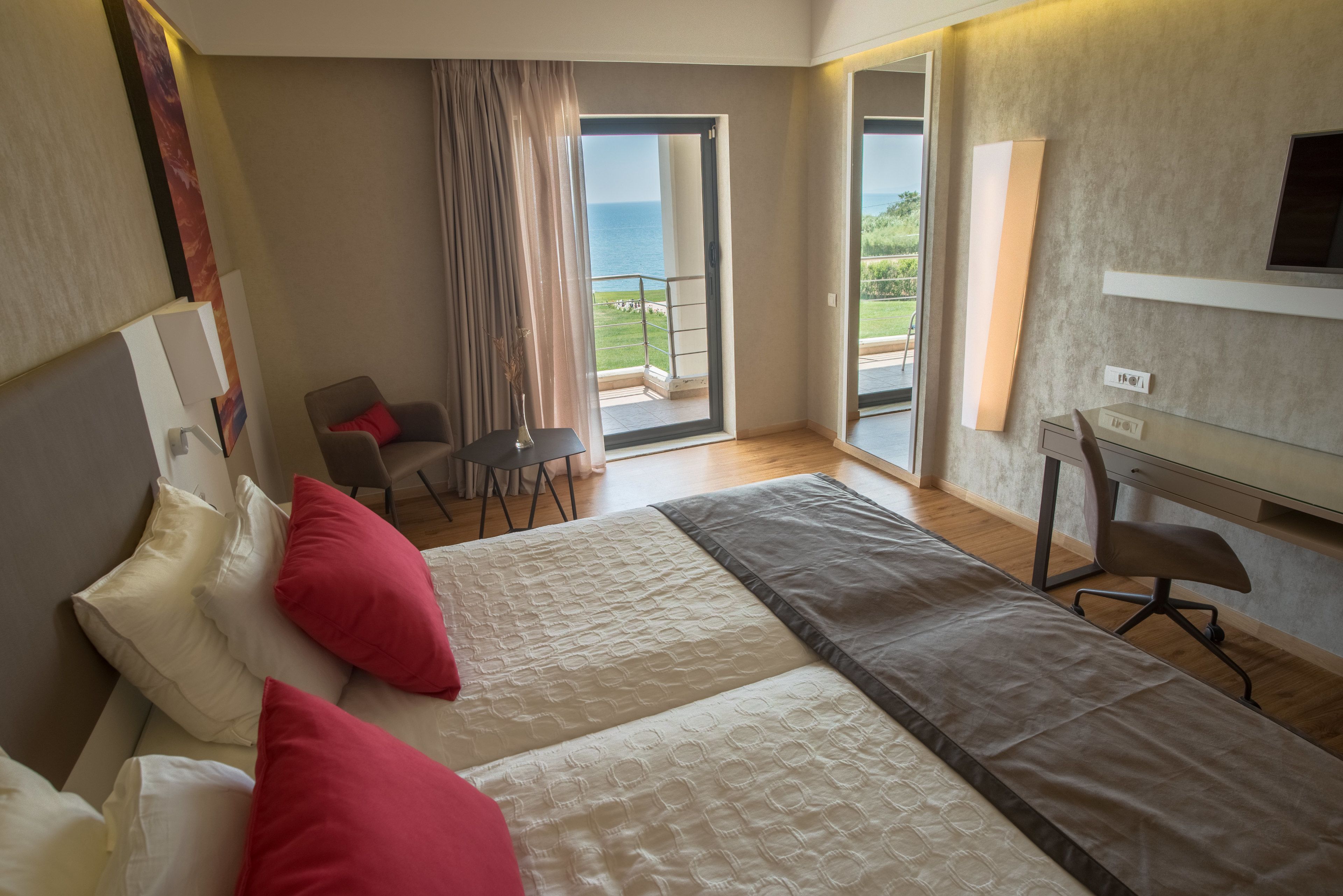 Habitación de hotel con cama, escritorio, silla y balcón con vista al mar.