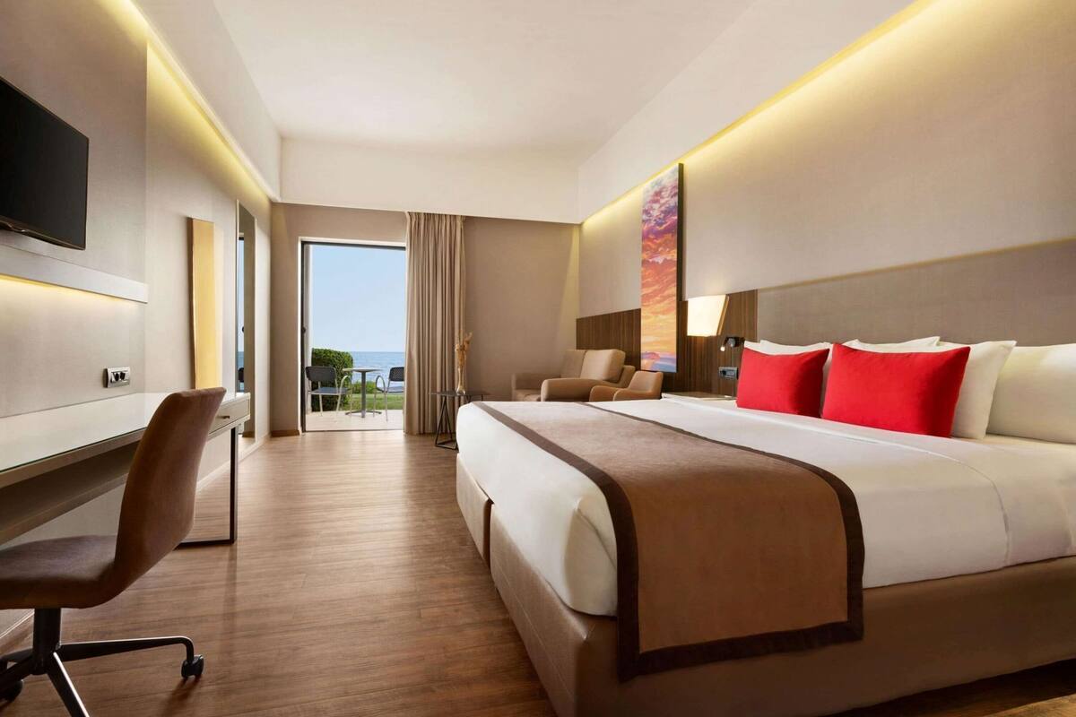 A hotel room with a bed, desk, chair, and a view of the outdoors.