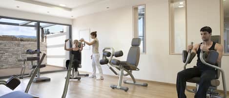 A modern gym with exercise equipment, large windows, and a stone wall.