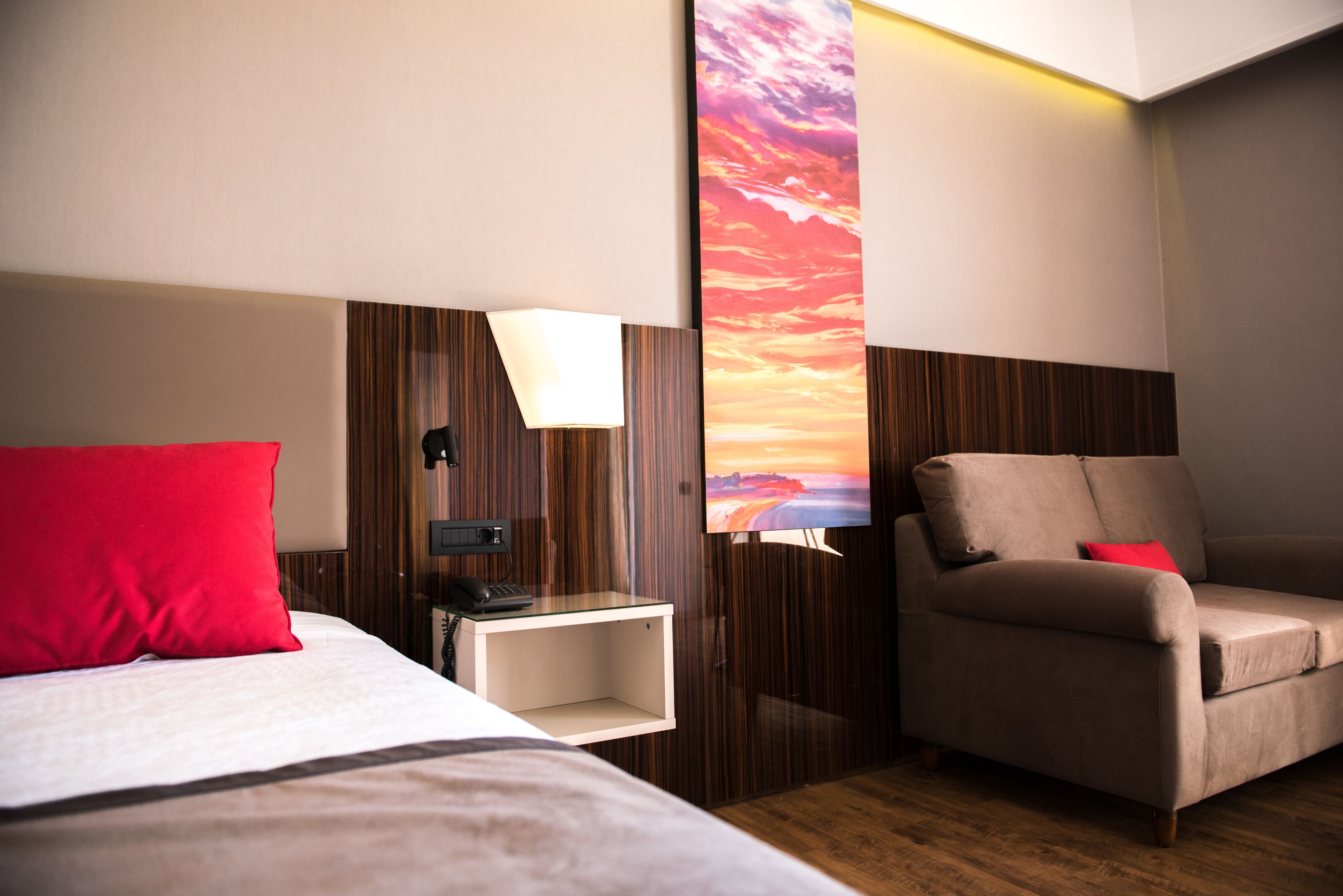 A hotel room with a bed, a desk, a chair, and a TV displaying a sunset view.