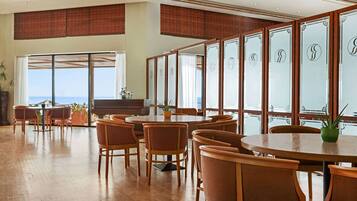 A spacious dining area with round tables and chairs, large windows with a view of the ocean, and a modern interior design.