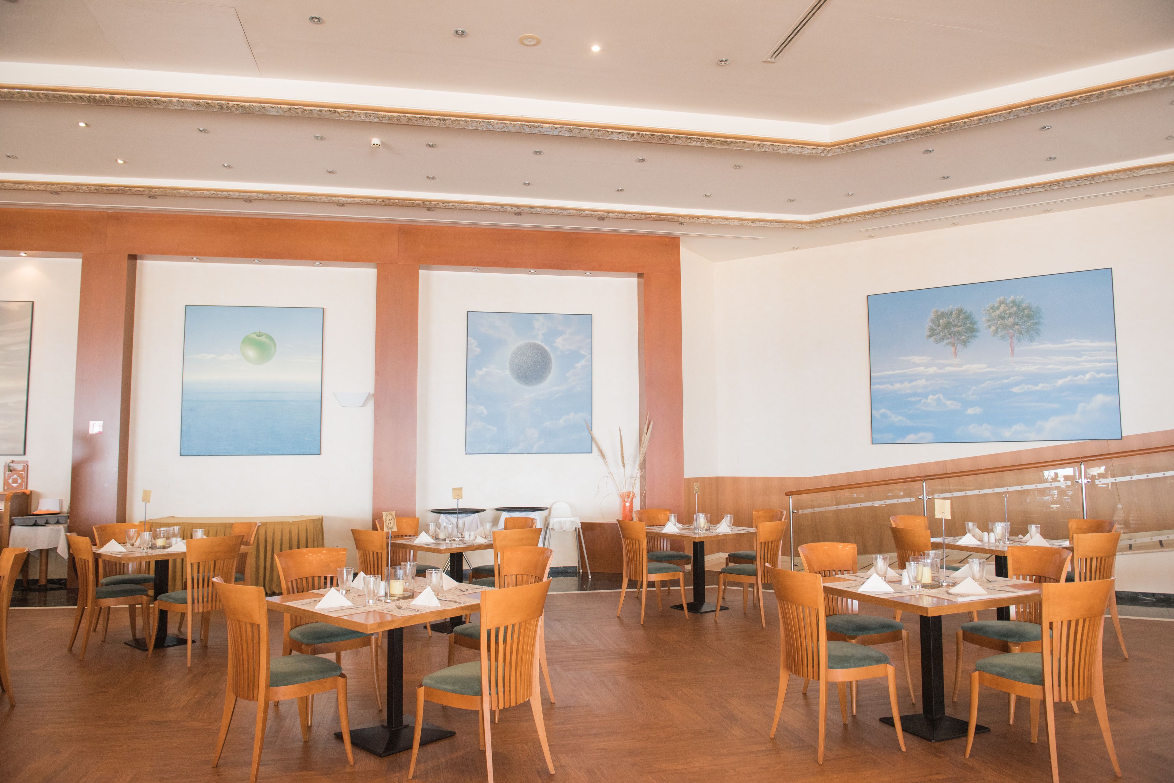 Un restaurant avec des tables et des chaises en bois, des œuvres d’art encadrées accrochées aux murs et un escalier en arrière-plan.