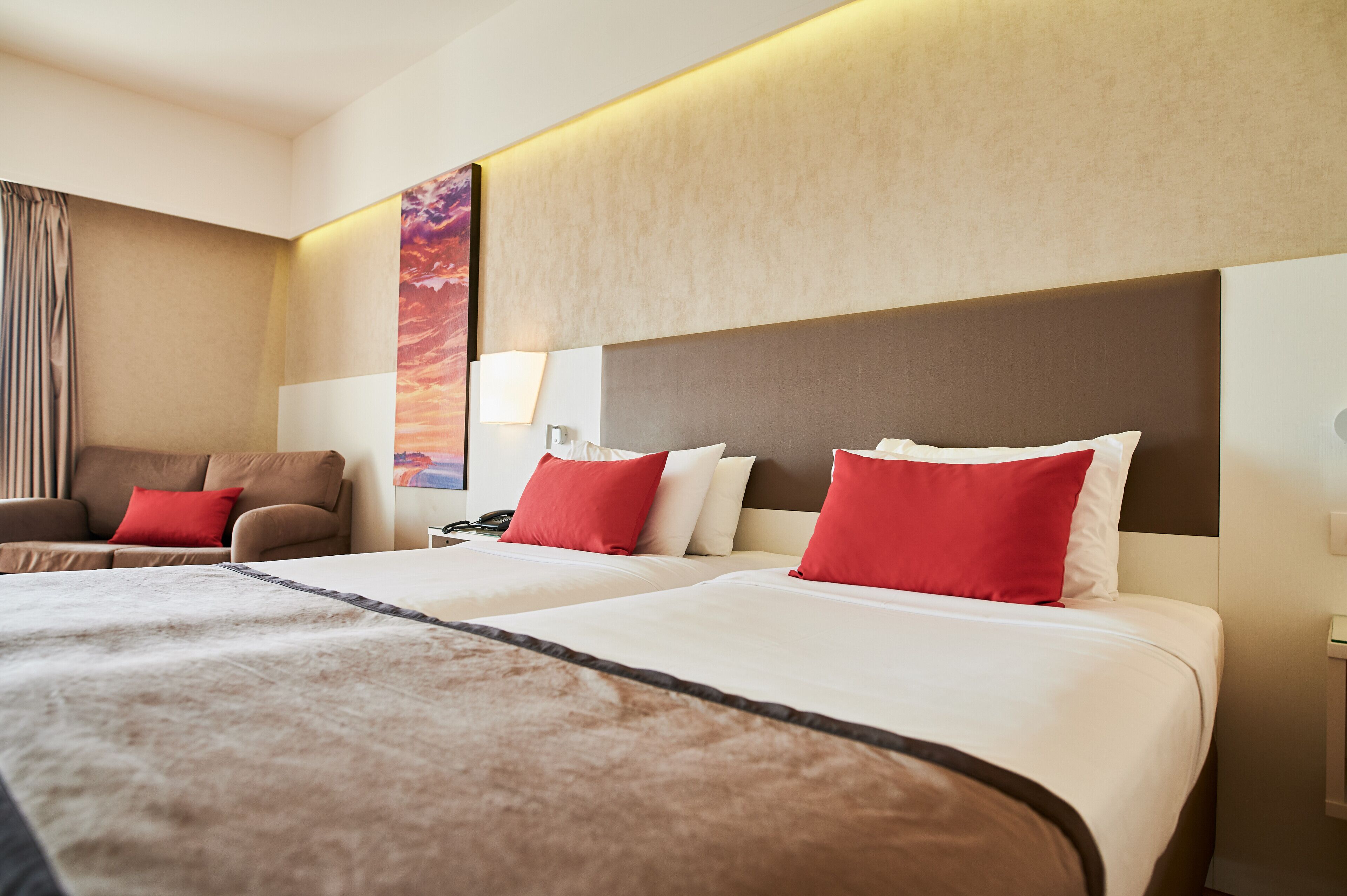 Habitación de hotel con dos camas, un sofá y un cuadro grande en la pared.