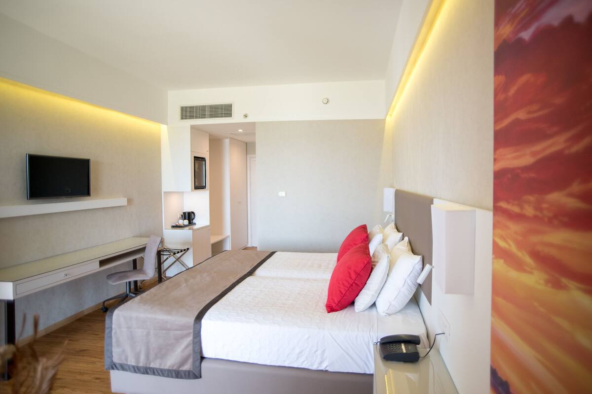 A modern hotel room with a bed, bedside table, TV, desk, and chair.