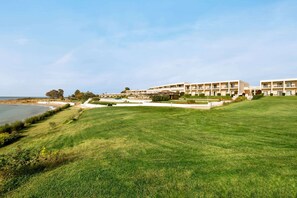 A coastal hotel with multiple buildings, a well-maintained lawn, and a view of the sea.