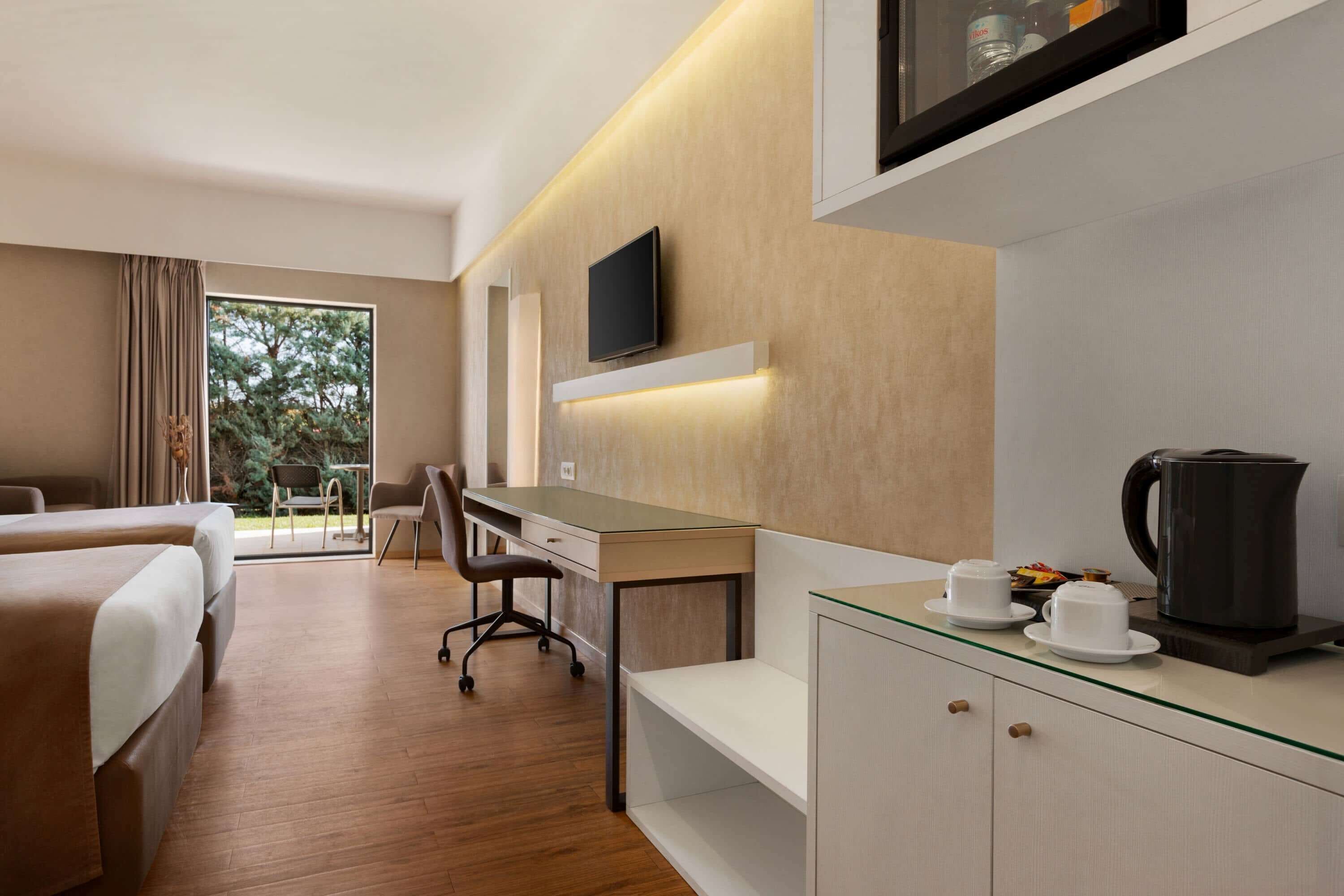 A modern hotel room with a bed, desk, chair, and a coffee station.