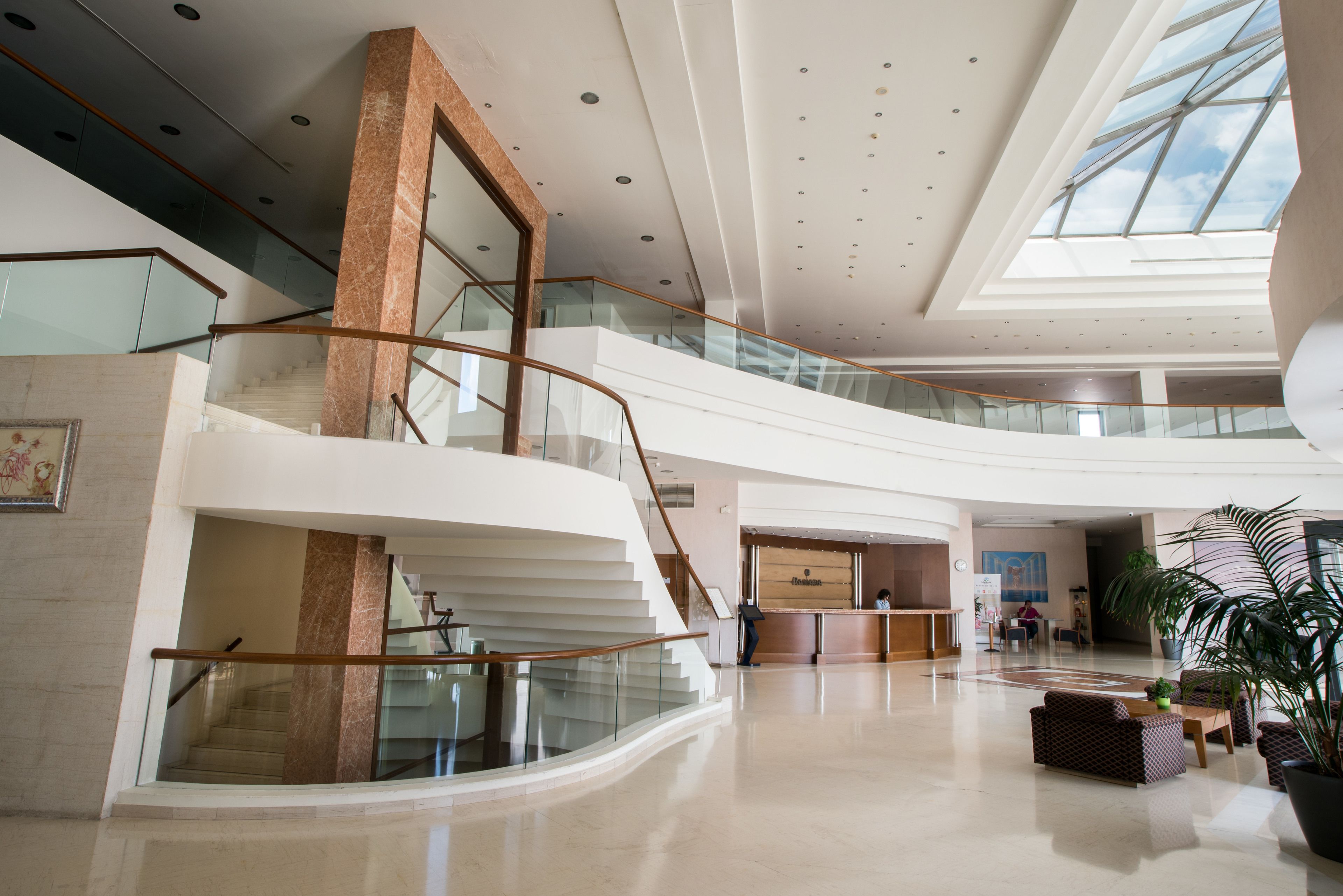 A spacious lobby with a central staircase, a reception desk, and a large potted plant.
