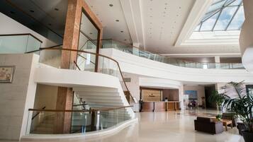 A spacious lobby with a central staircase, a reception desk, and a large potted plant.