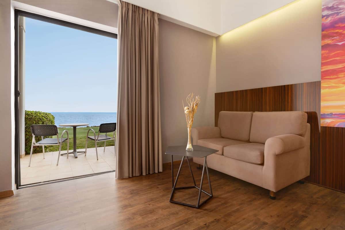 A modern living room with a sofa, a small table, and a view of the sea through a glass door.