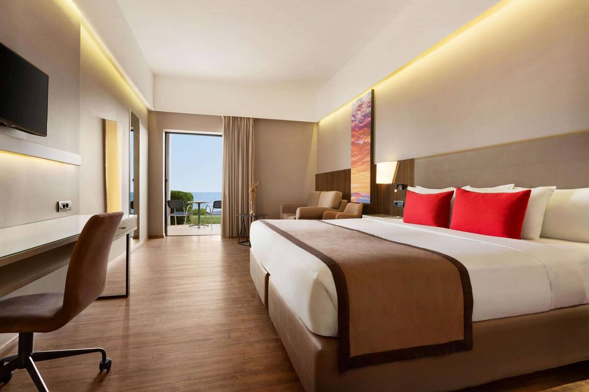 A hotel room with a large bed, a desk, a chair, and a TV mounted on the wall.