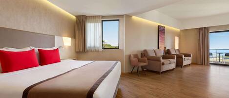 A hotel room with a large bed, a seating area with chairs, a large window, and a view of the outdoors.