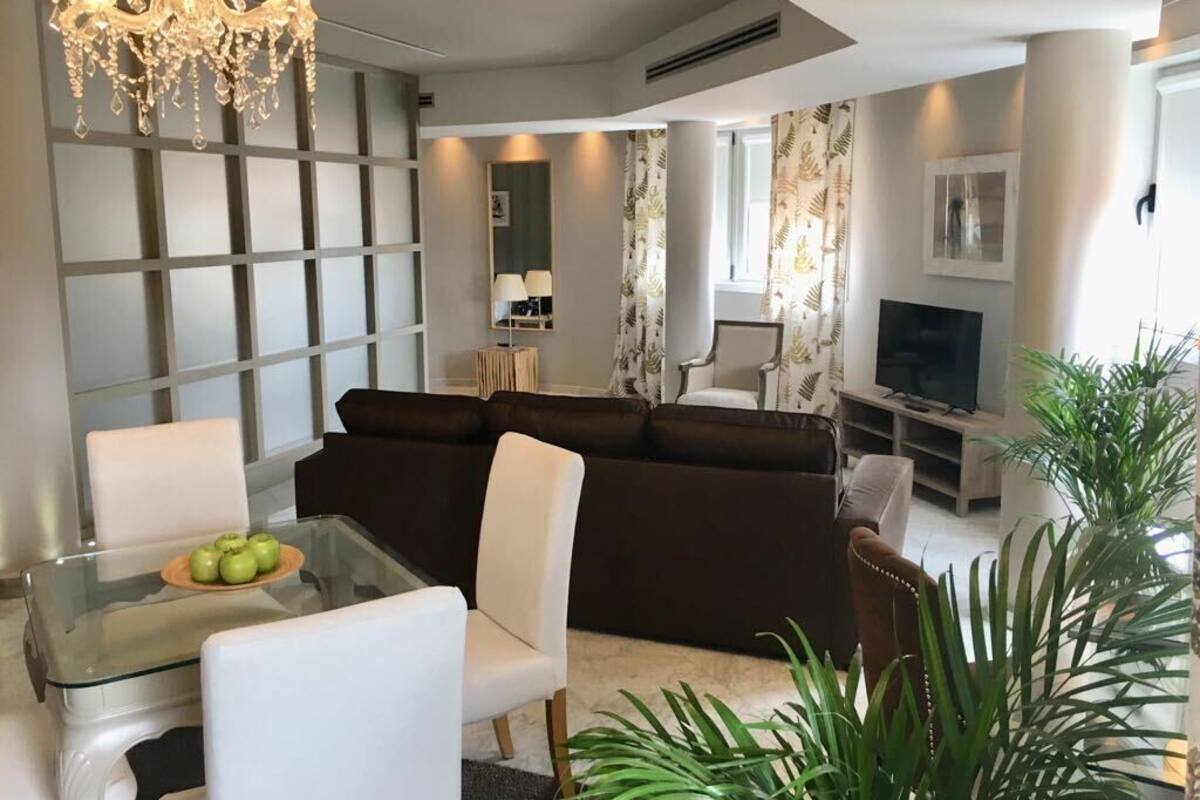 Un salon moderne avec un canapé d’angle, une table basse en verre, un téléviseur et un lustre.