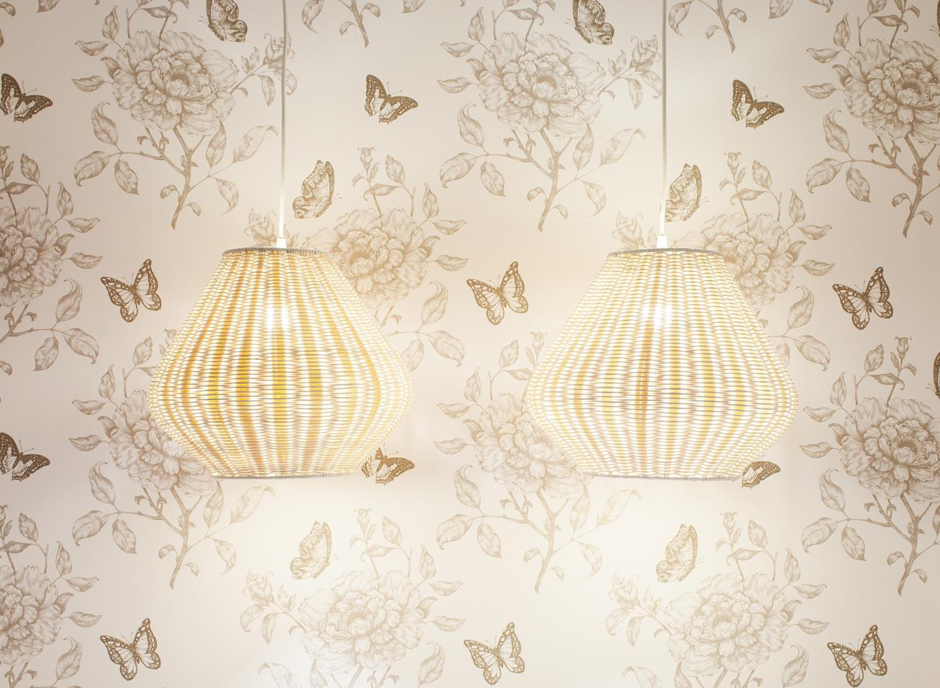 Two hanging lamps with a woven design against a floral wallpaper background.
