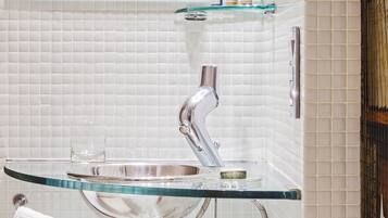 A bathroom with a glass sink, white tiled walls, and a mirror above the sink.