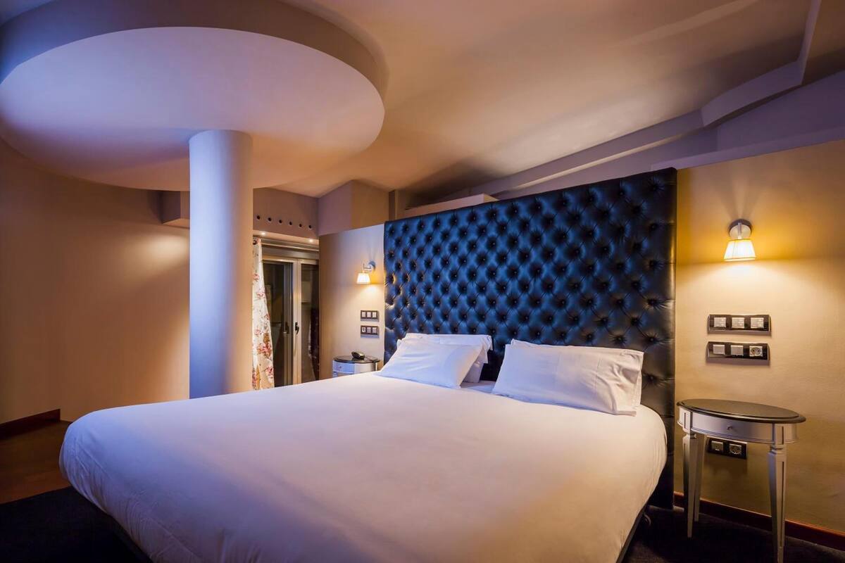 Une chambre d’hôtel avec un grand lit, une tête de lit capitonnée, deux lampes de chevet et une petite table d’appoint.