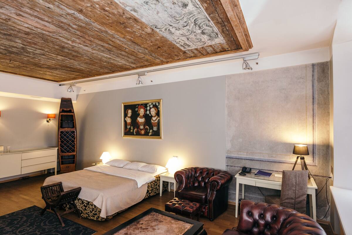 Ein Schlafzimmer mit einem Bett, zwei Stühlen, einem Schreibtisch und einem Bild an der Wand.