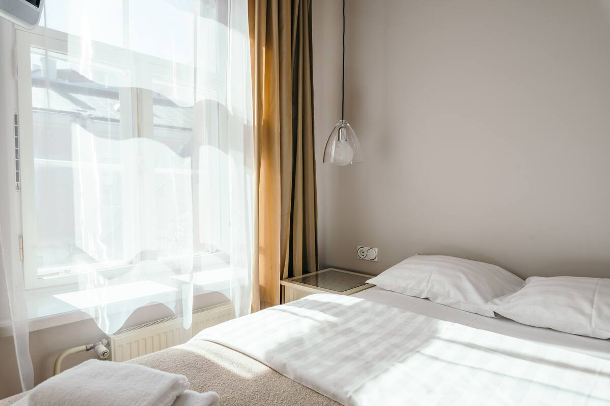 Ein Hotelzimmer mit einem Bett, einem Nachttisch, einem Fenster mit Vorhängen und einer Wandlampe.