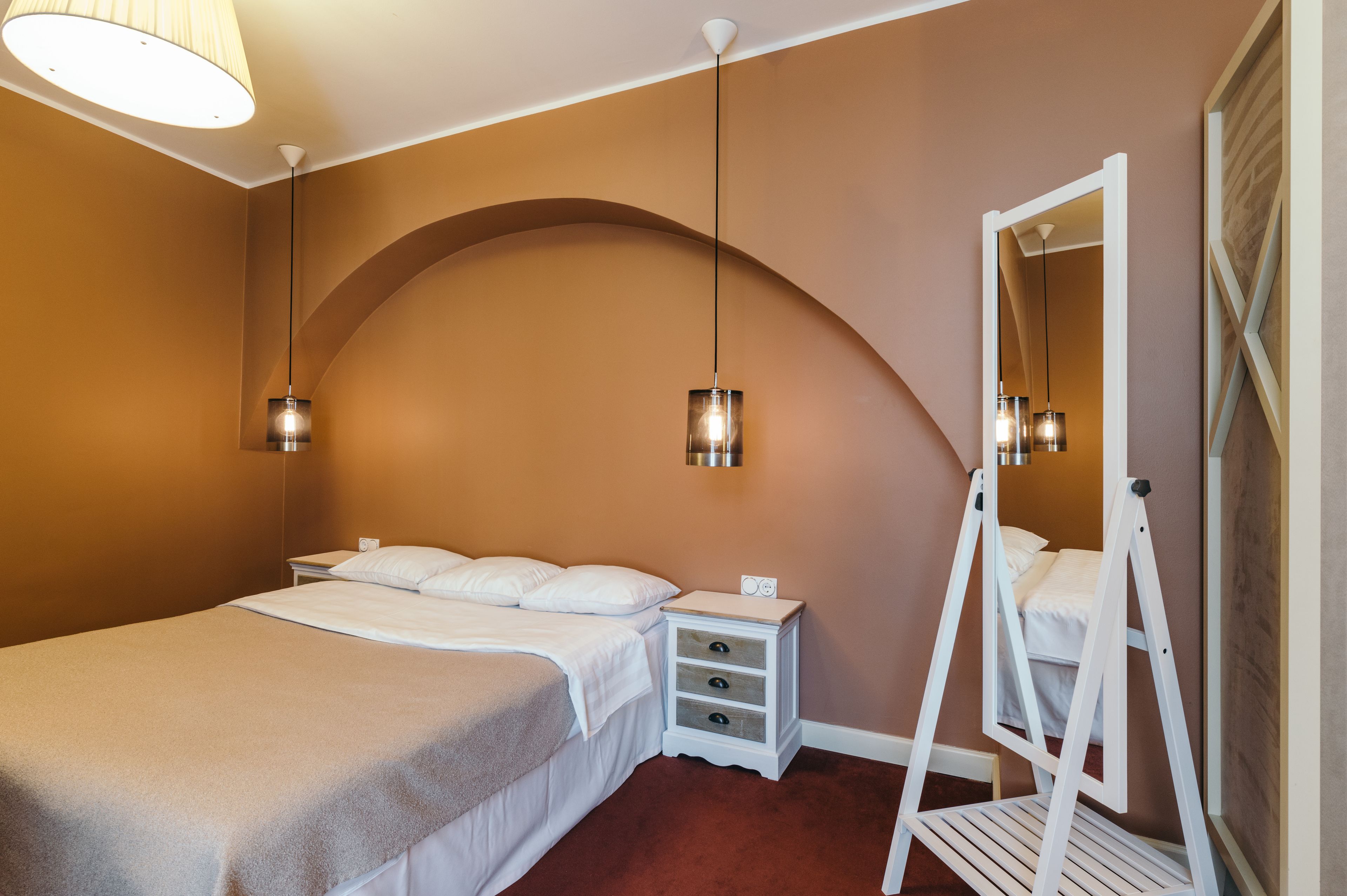 A bedroom with a bed, bedside tables, a mirror, and a hanging light fixture.