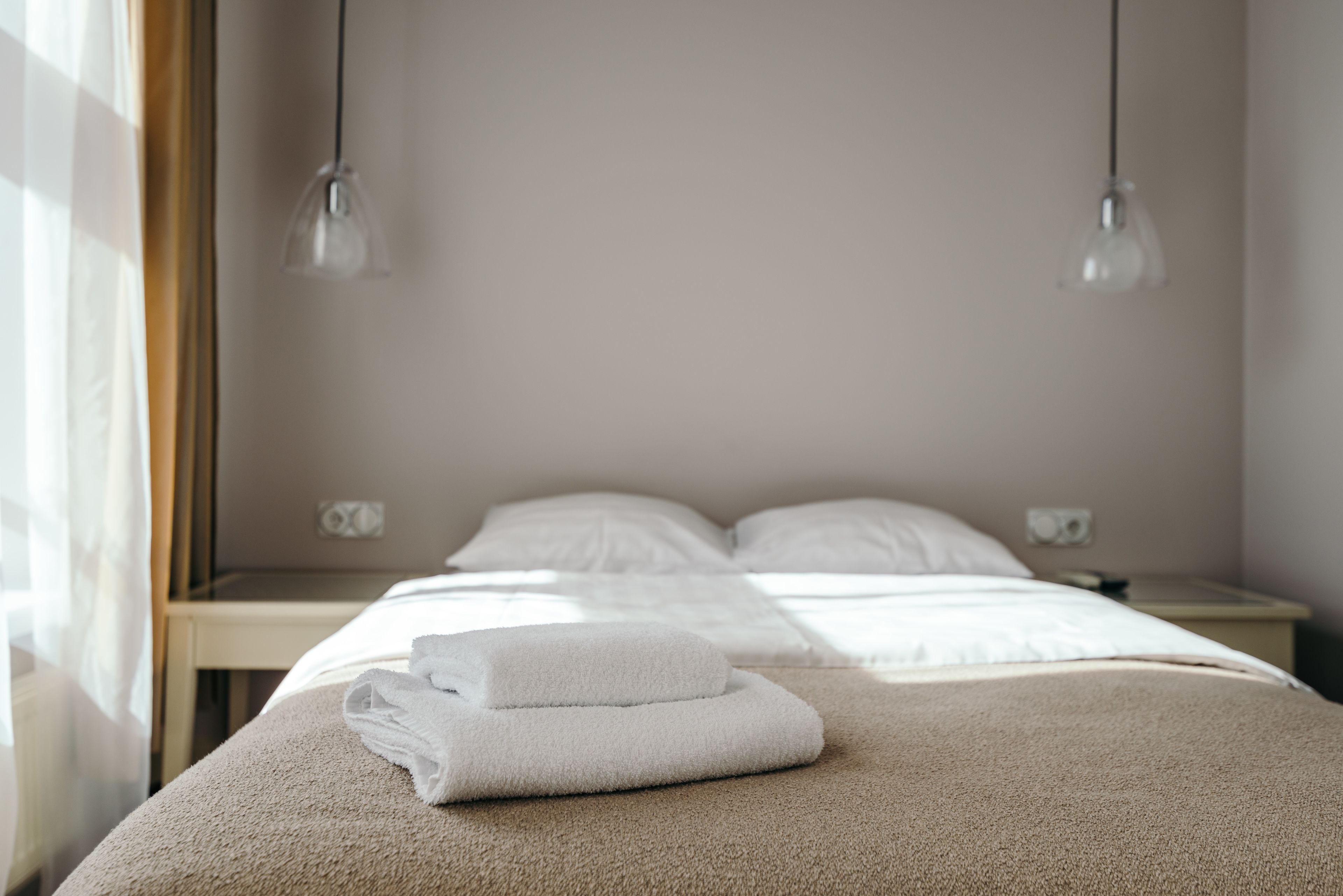 Une chambre d’hôtel avec un lit soigneusement fait, une serviette pliée posée sur le lit et deux lampes suspendues au plafond.