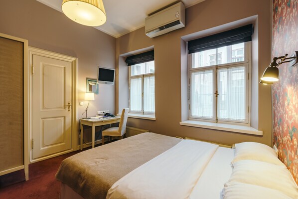 Una habitación de hotel con una cama, un escritorio, una silla, un televisor y dos ventanas.