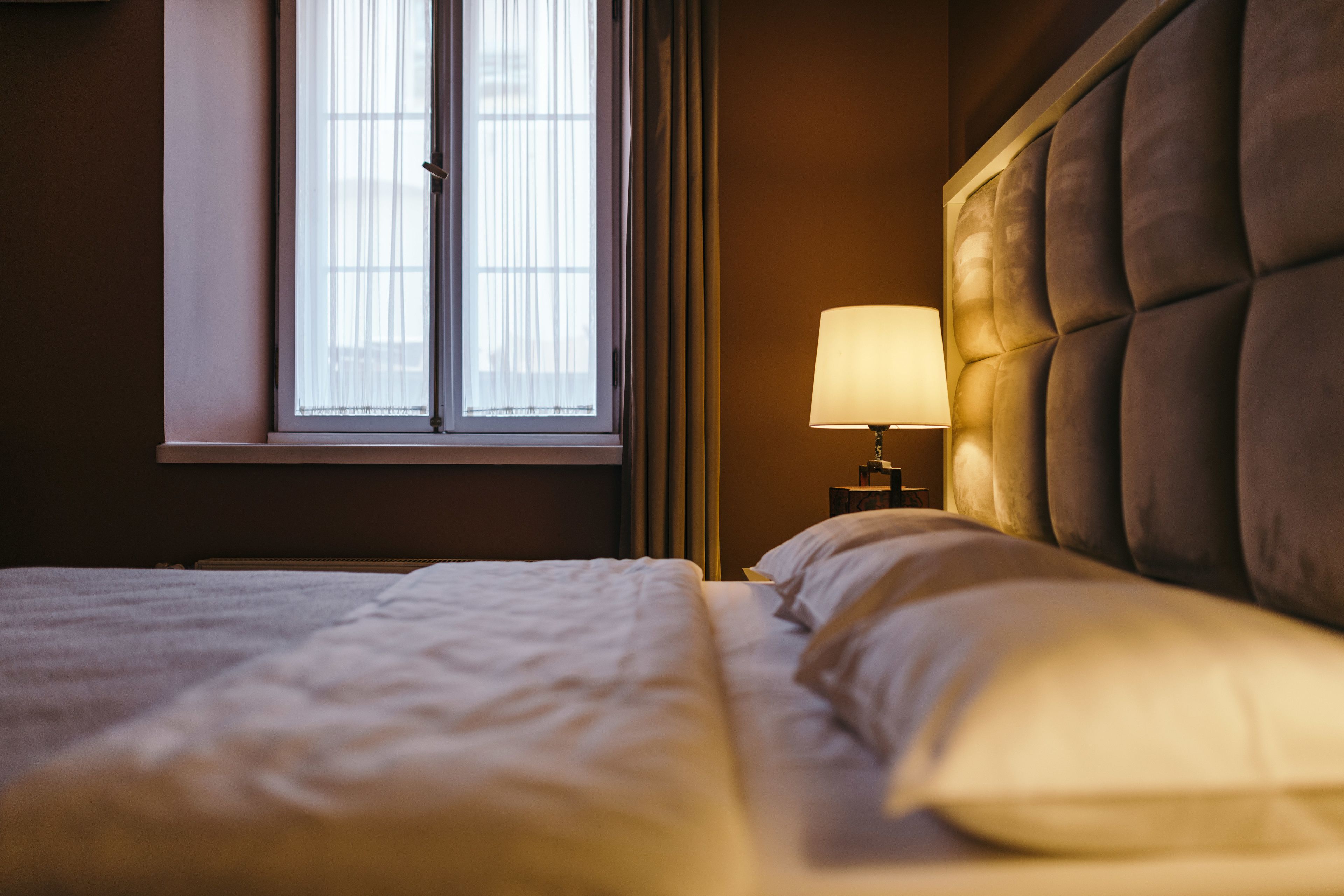A hotel room with a bed, a window with curtains, and a bedside lamp.