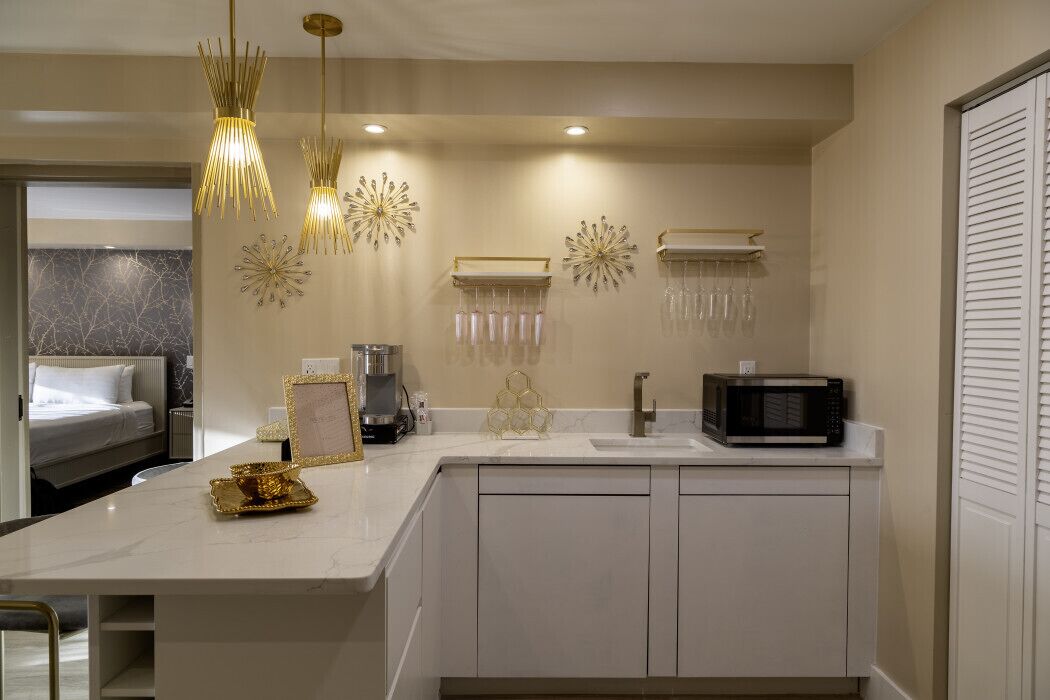 A modern kitchen with a white countertop, a microwave, hanging light fixtures, and decorative wall art.