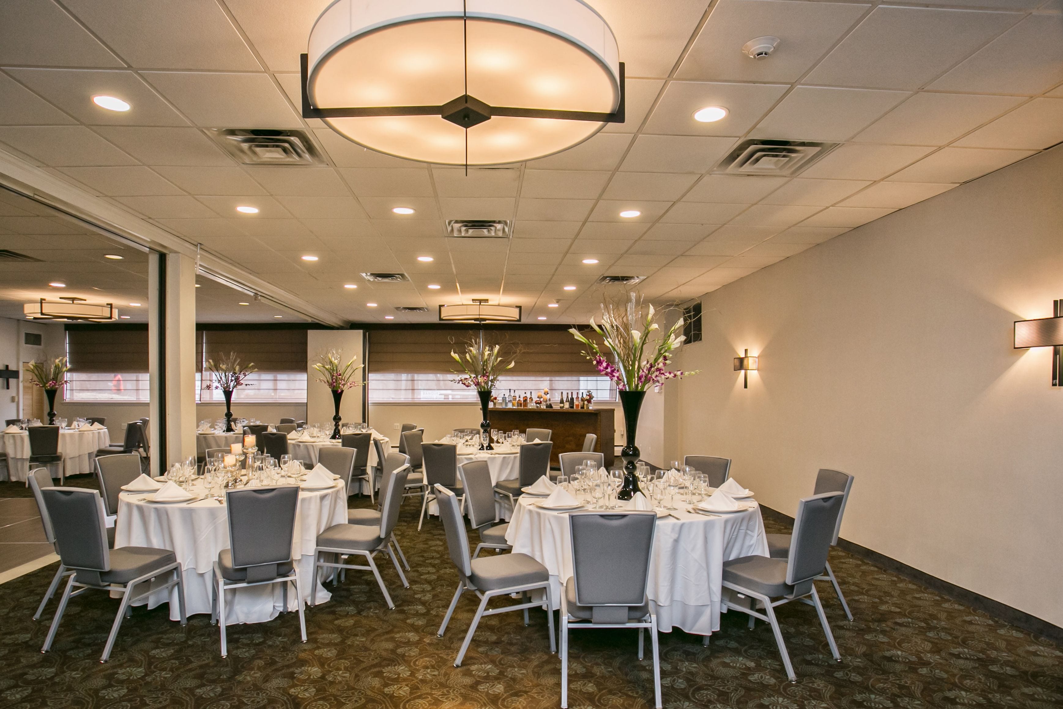 A banquet hall with round tables set for dining, featuring white tablecloths and grey chairs.