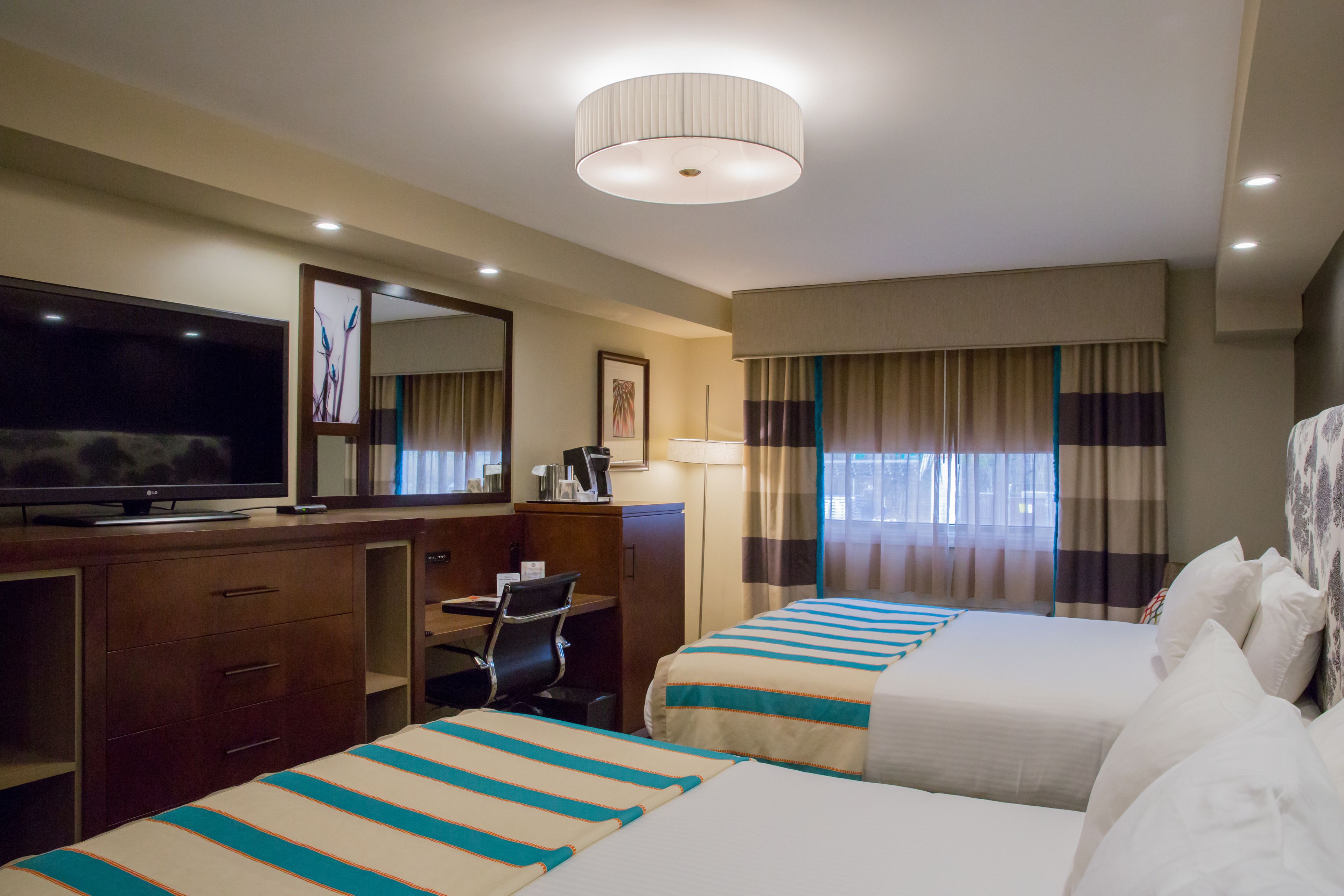 A hotel room with two beds, a desk, a television, and a large mirror.