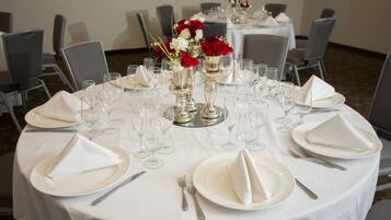A round table set for a formal event with white tablecloths, silverware, and glassware.